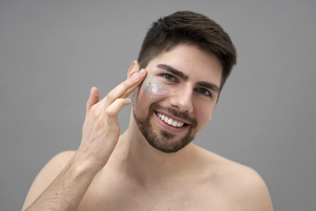 Young man with beard applying SPF lotion or sunscreen to his face as third step of daily skincare protection routine