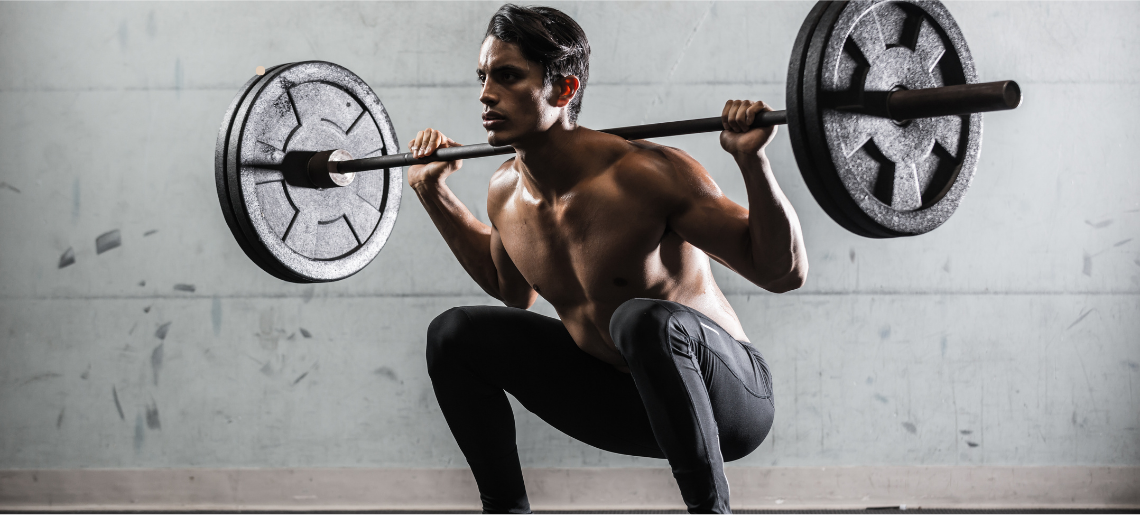 Muscular man performing barbell back squat with heavy weights in gym, demonstrating proper strength training form and technique