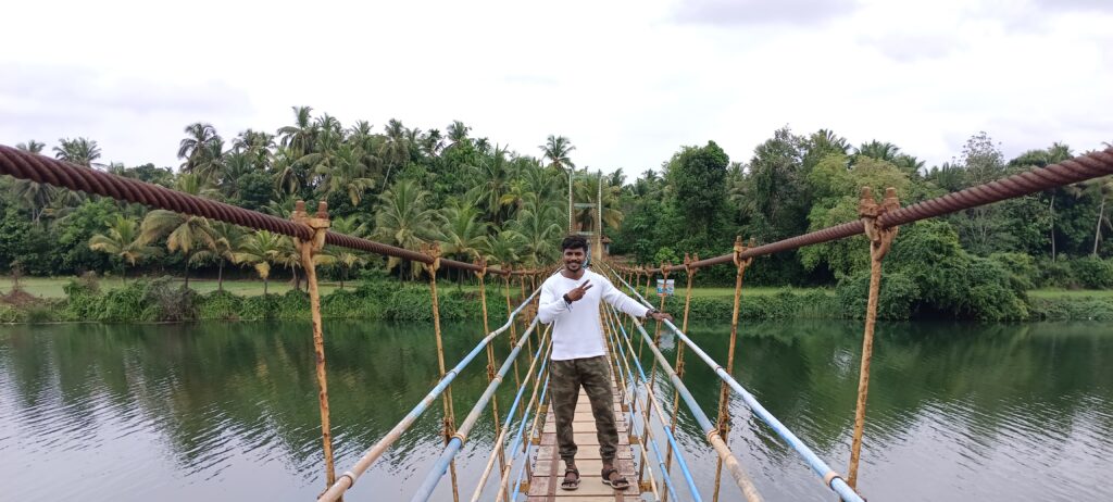 Traveler standing on wooden hanging bridge over backwaters surrounded by lush green mangrove forest in Udupi, Kerala