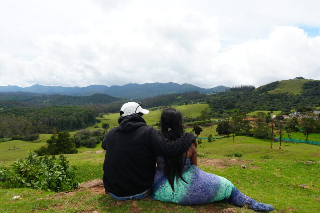 Couple sitting on a grassy hill overlooking the Nilgiri mountains in Ooty on their babymoon